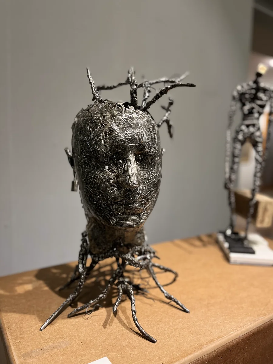 A sculpture of a human head made of tangled wire, on a wooden plinth